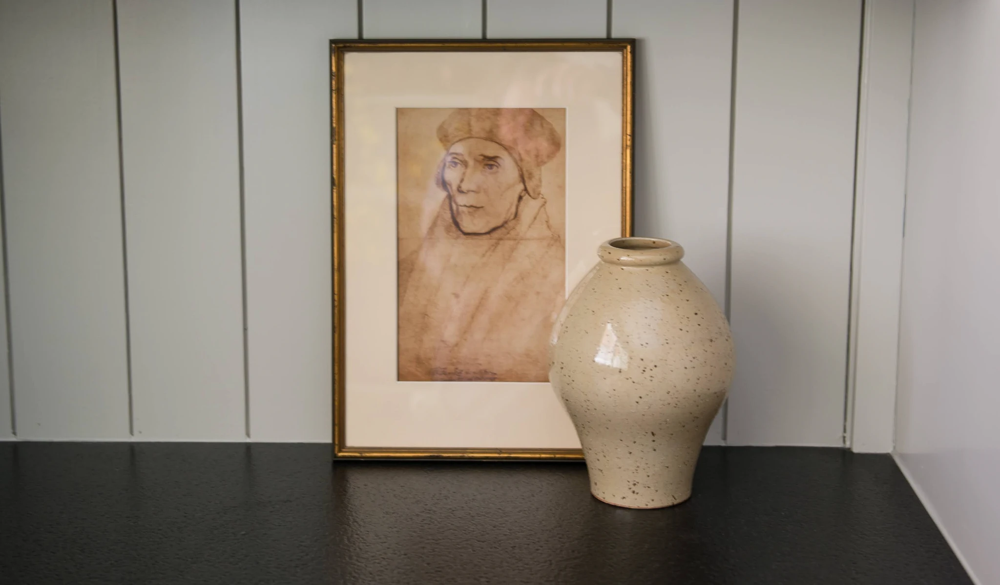 A vase sits on a table next to a painting in a home.