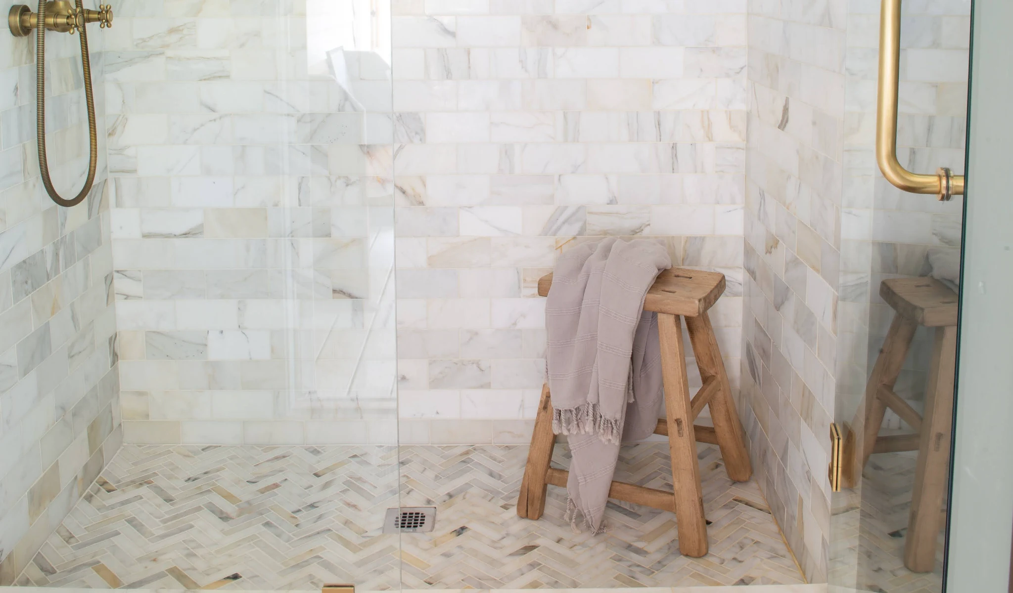 A white tiled shower with a wooden stool.