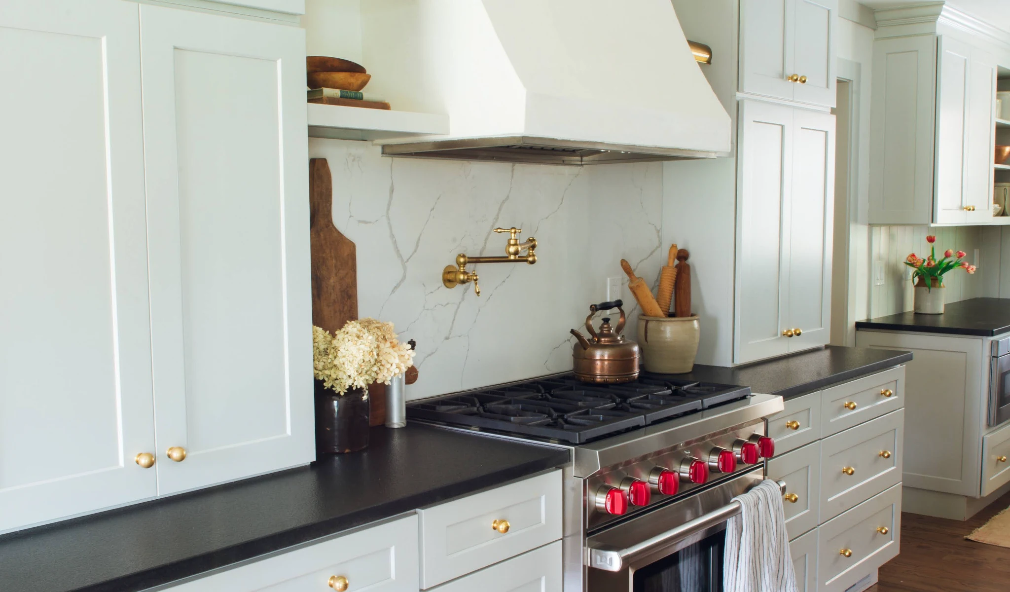 A kitchen with white cabinets, a new stove, and gold accents.