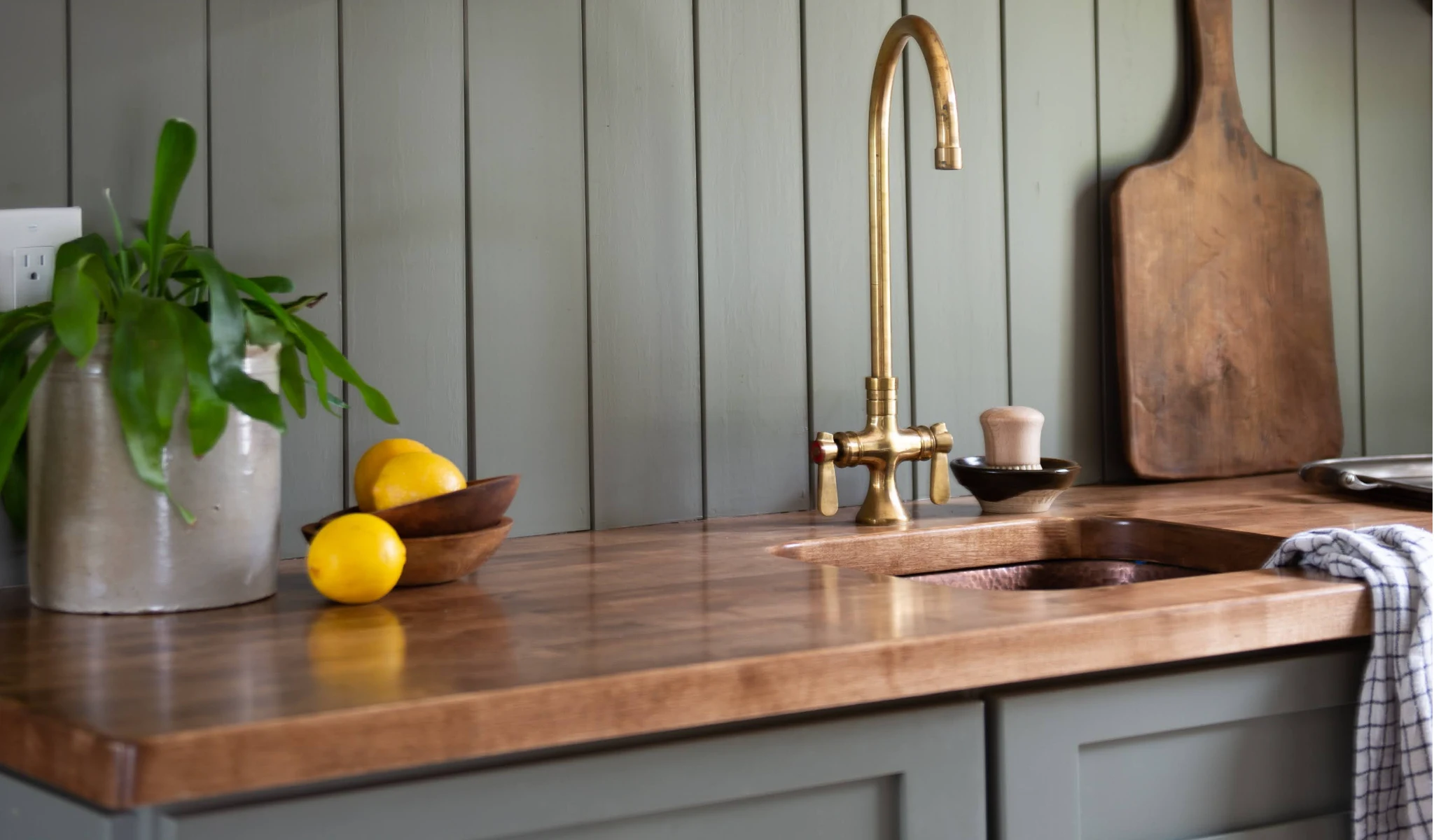 A wooden kitchen counter and sink with a brass faucet.