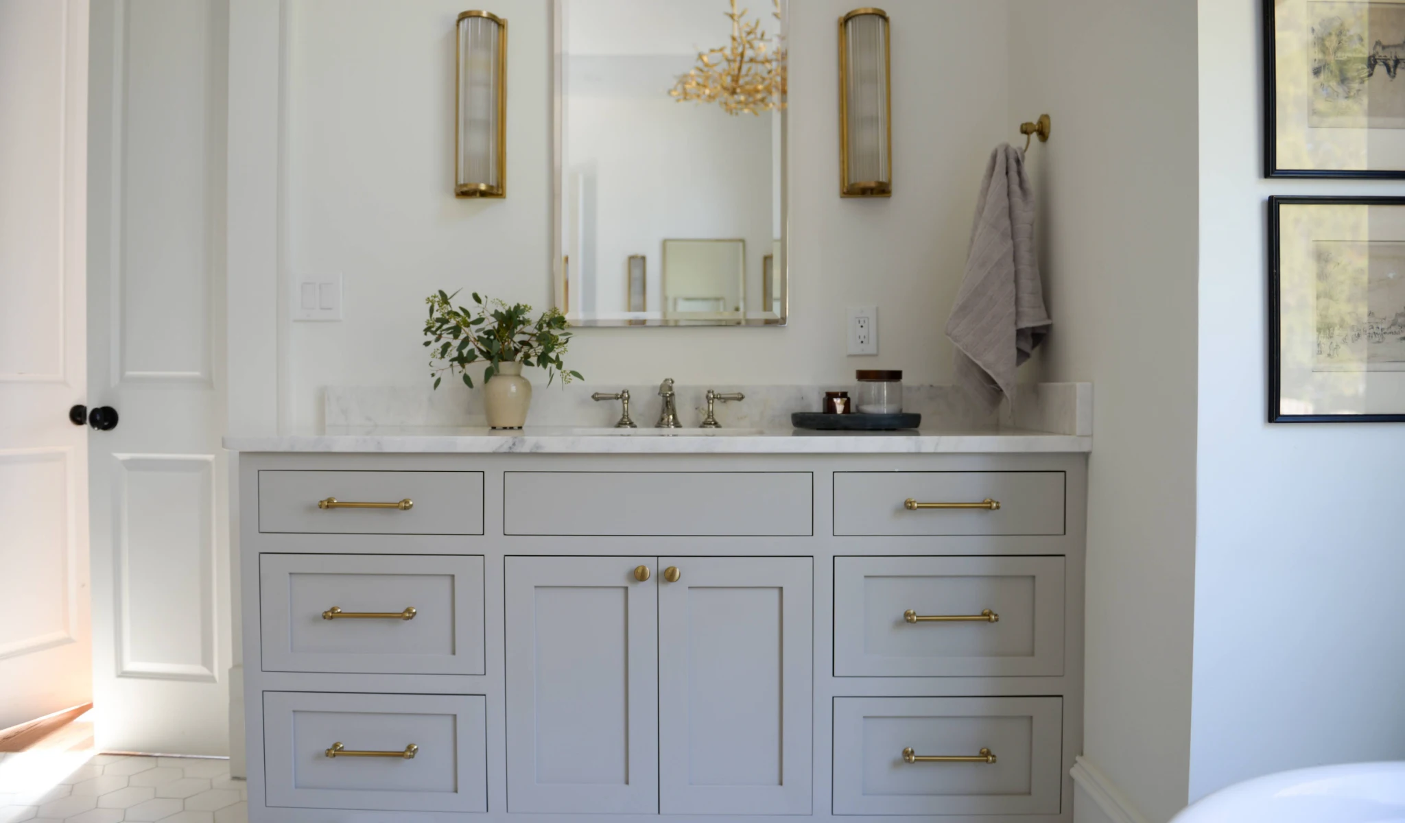 A bathroom with a white vanity and gold hardware designed by a home designer.