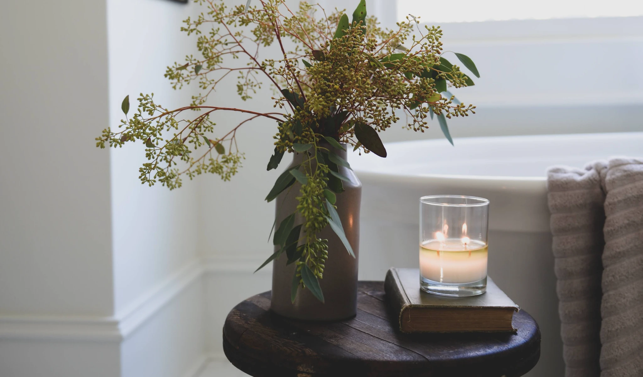 A candle sits on a wooden stool next to a bathtub in a custom home.