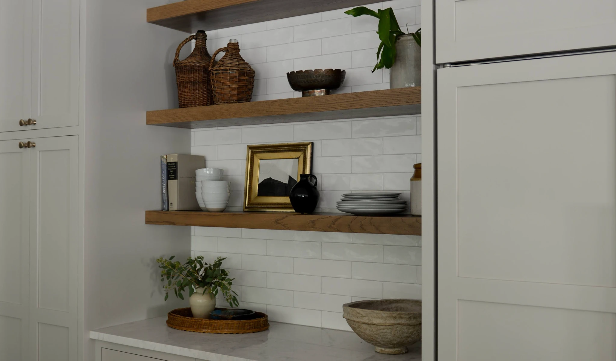 A white kitchen with wooden shelves and a potted plant.