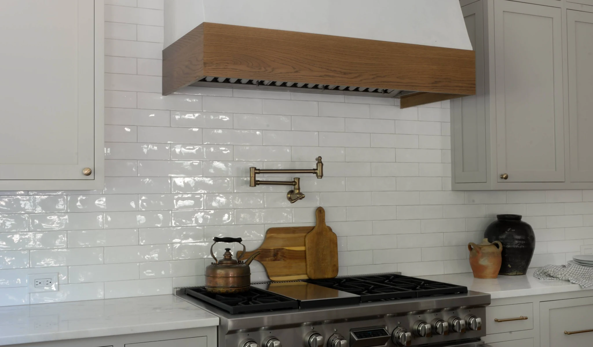 A white tiled kitchen with a wooden stove hood designed by home builders.