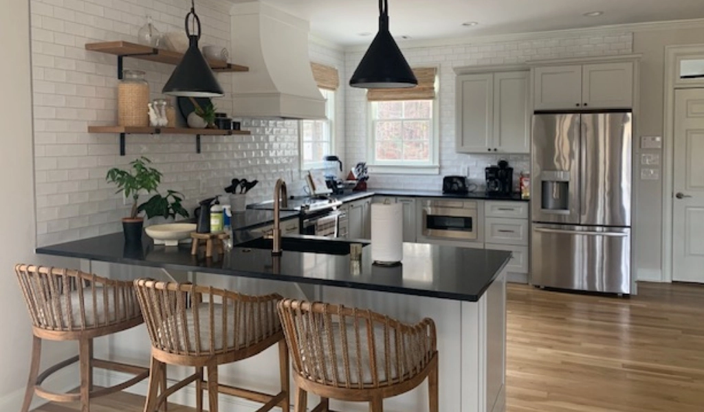 A kitchen with white cabinets and black countertops with wooden stools.
