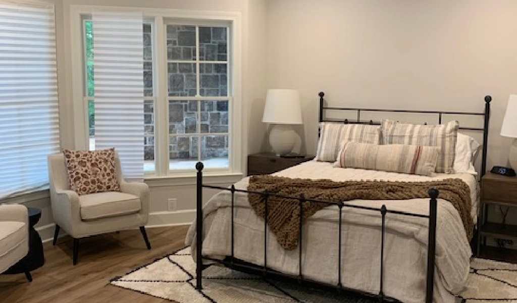 A bedroom with a bed and a chair next to a window.