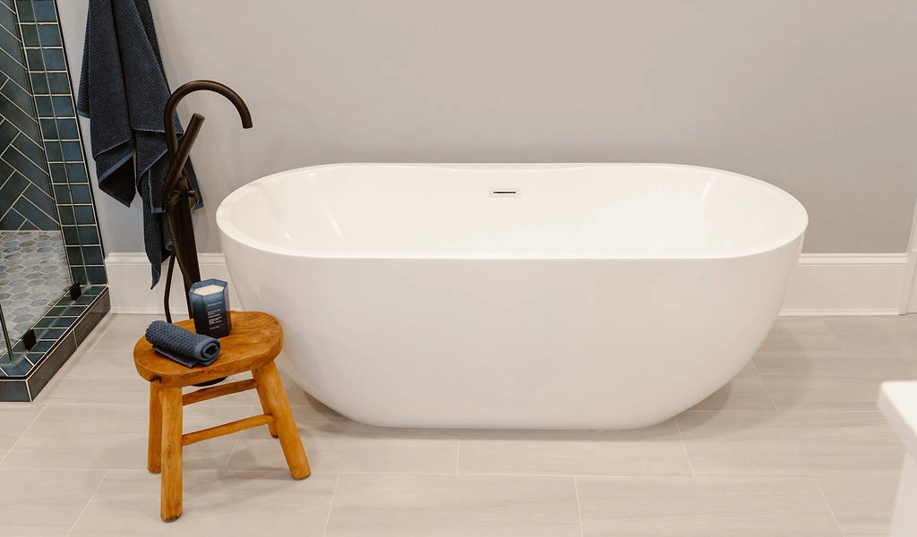 A white bathtub in a bathroom with a stool next to it.