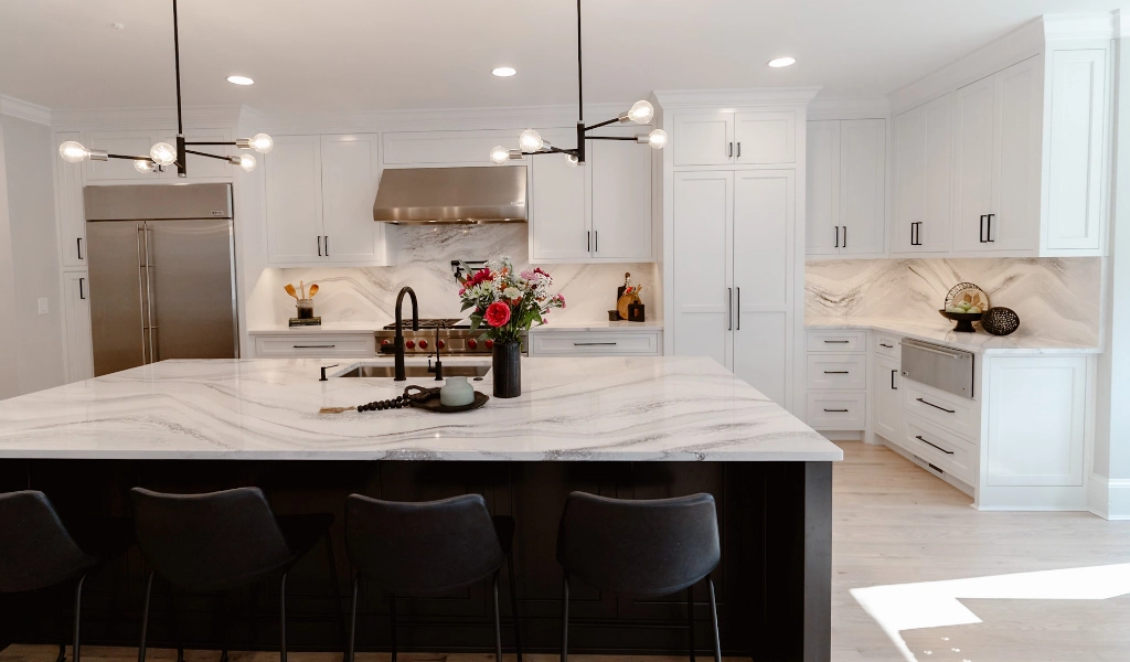 A white kitchen with marble counter tops and black chairs.