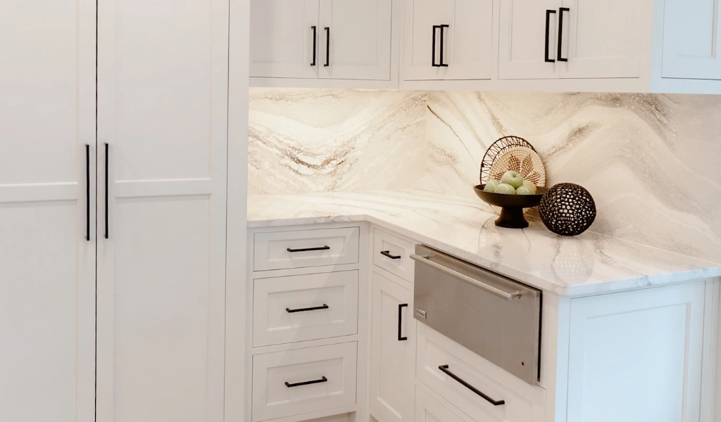 A modern kitchen with white cabinets and marble countertops.