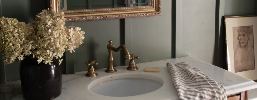 A bathroom with green walls and a gold mirror.