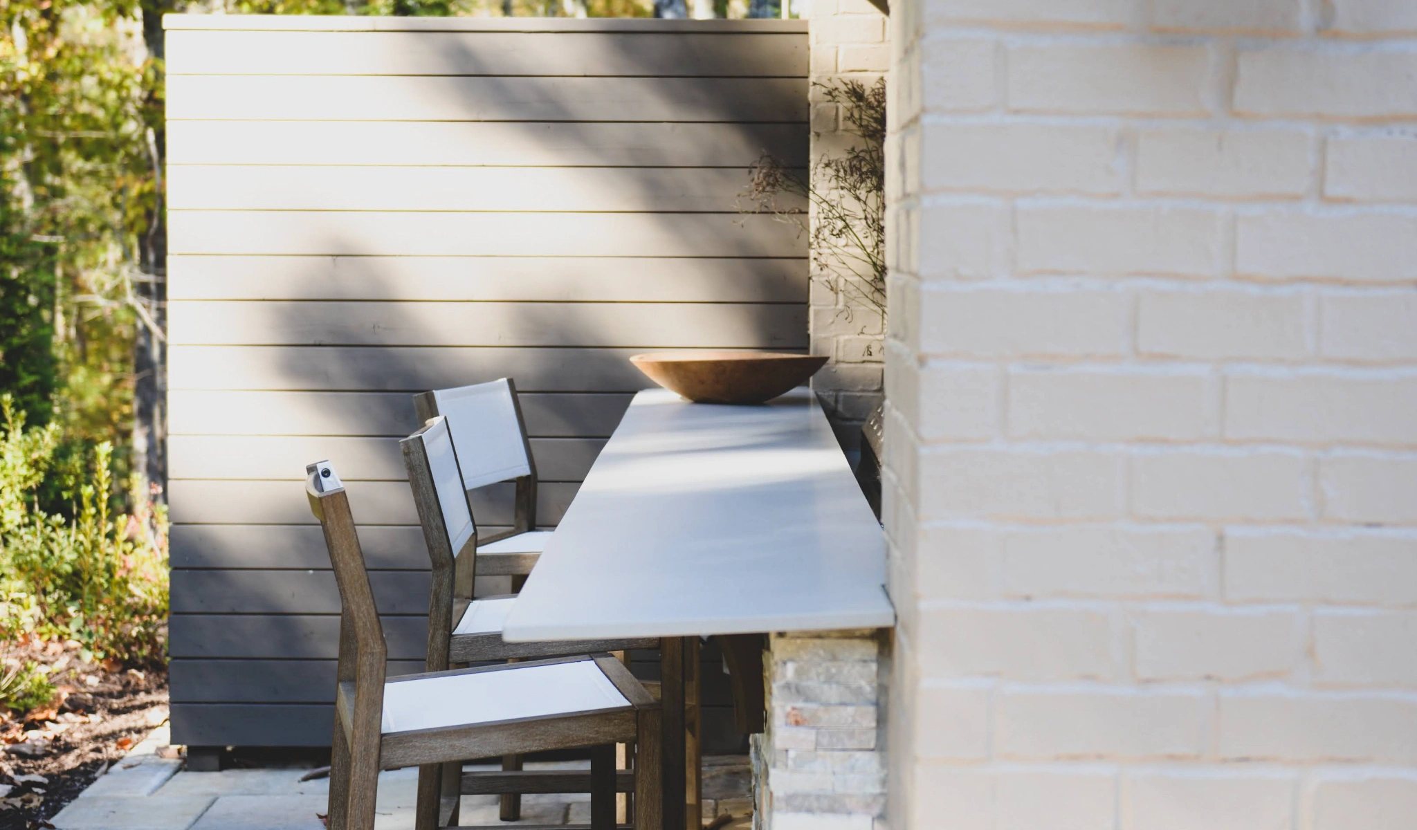 An outdoor bar with white chairs and a brick wall.