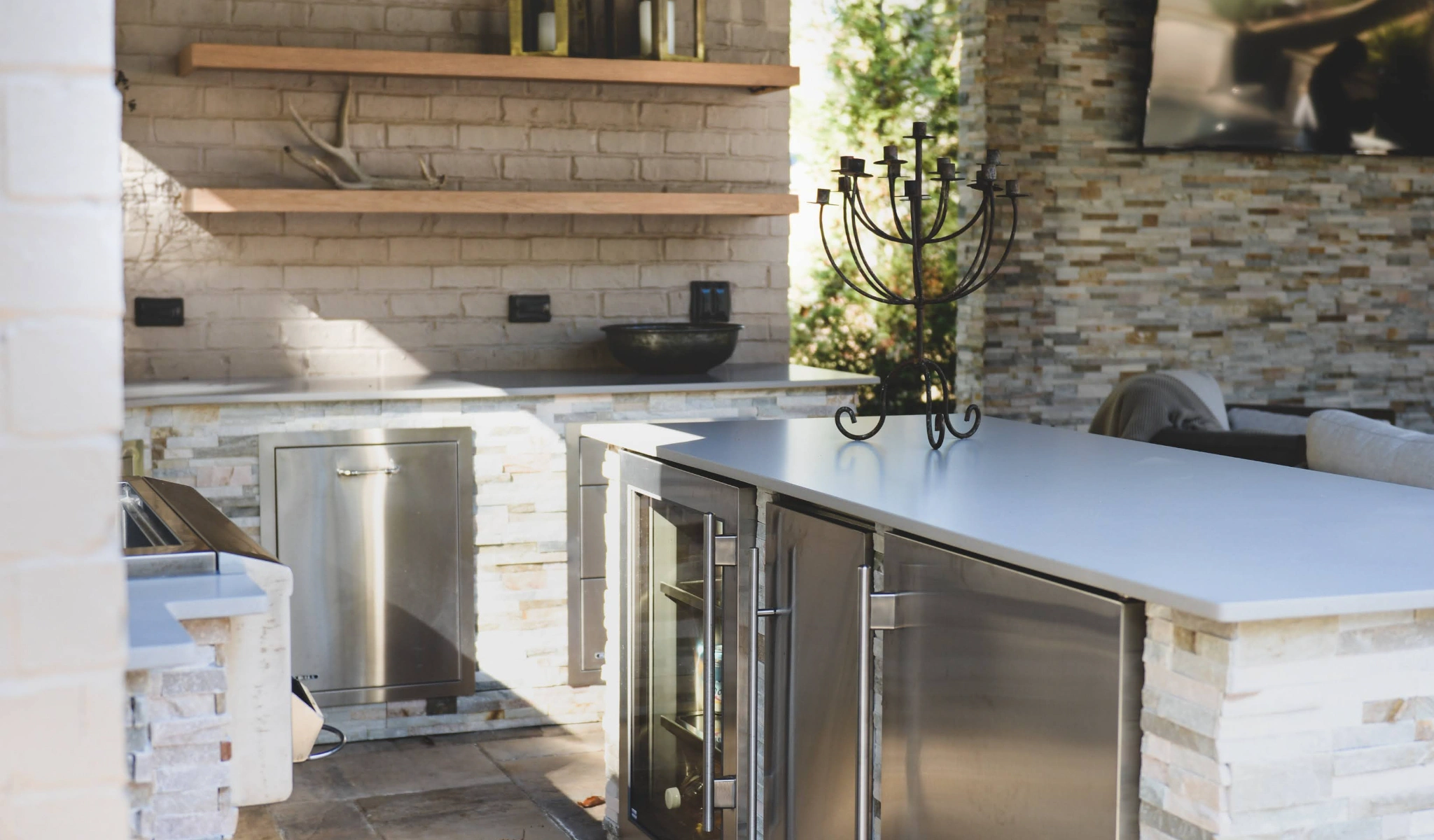 An outdoor kitchen with stainless steel appliances designed by a home designer.