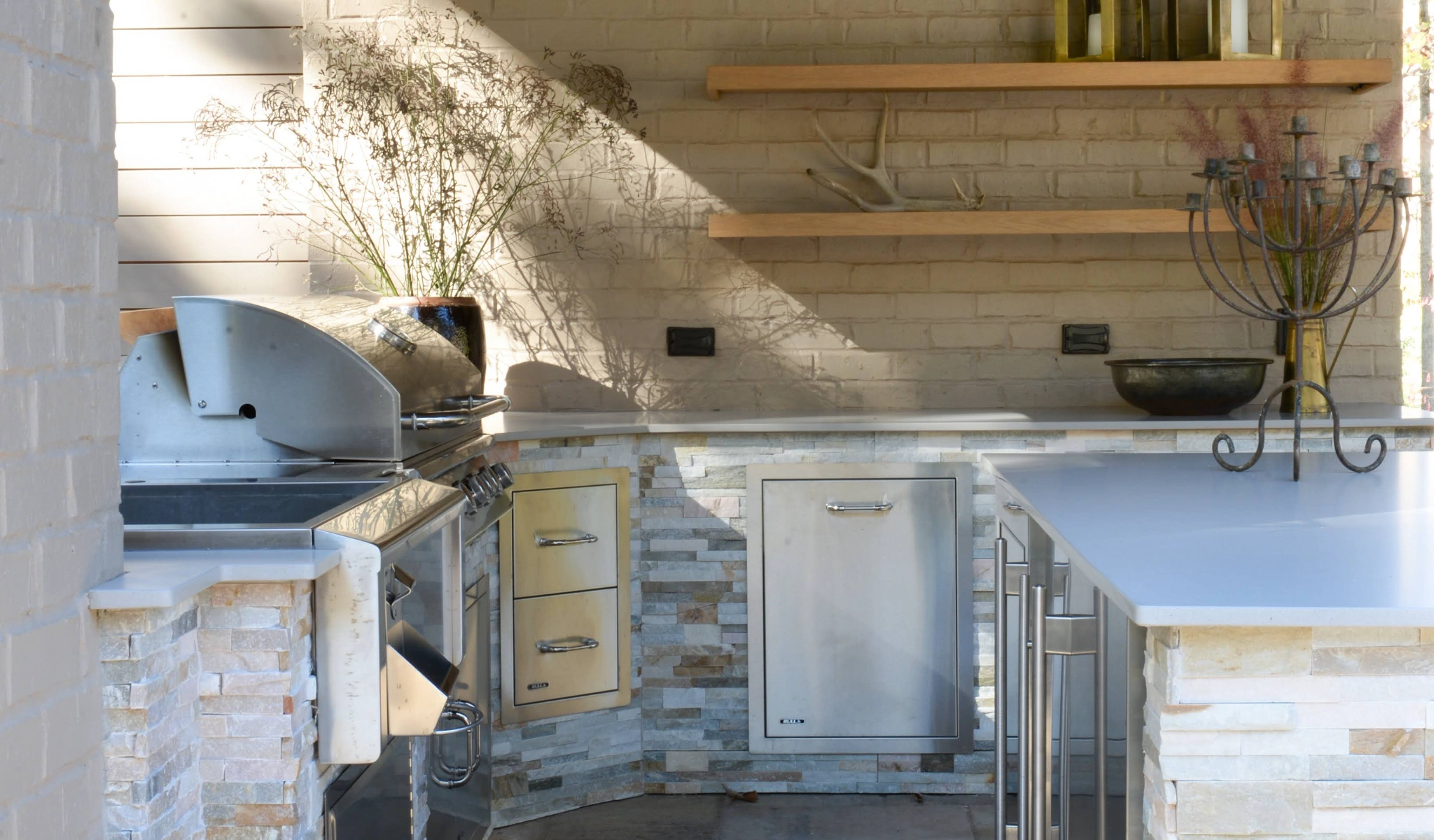 Outdoor kitchen featuring a grill and wooden shelves.