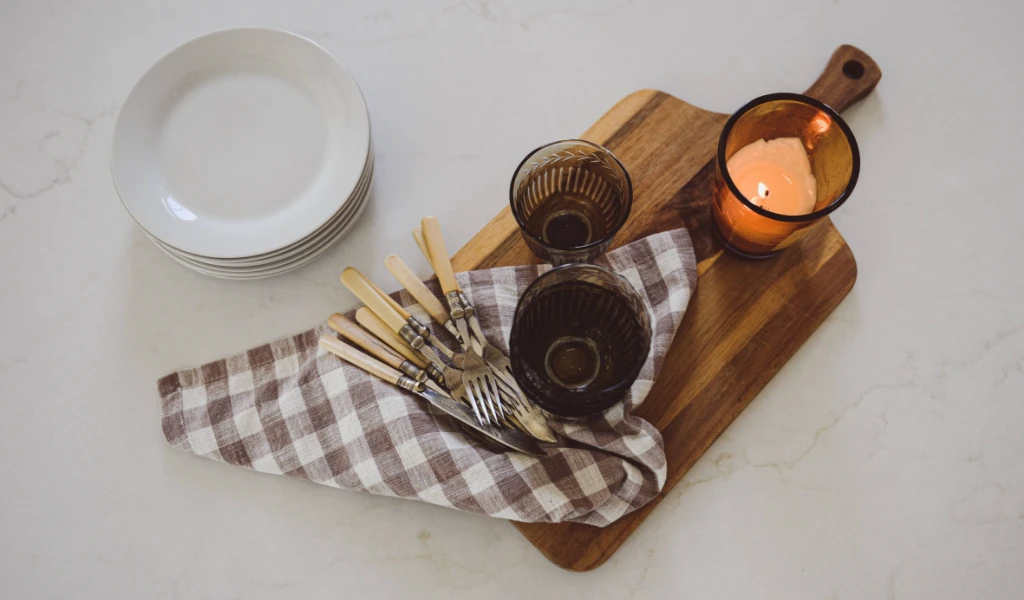 A wooden cutting board with utensils and a candle.