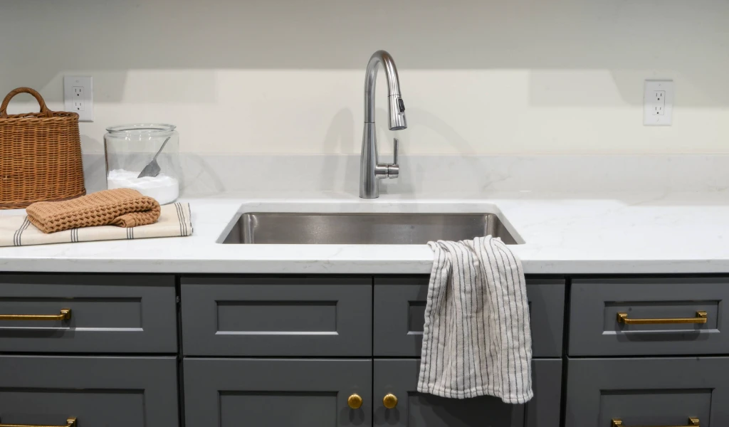 A laundry room with gray cabinets and a new sink.