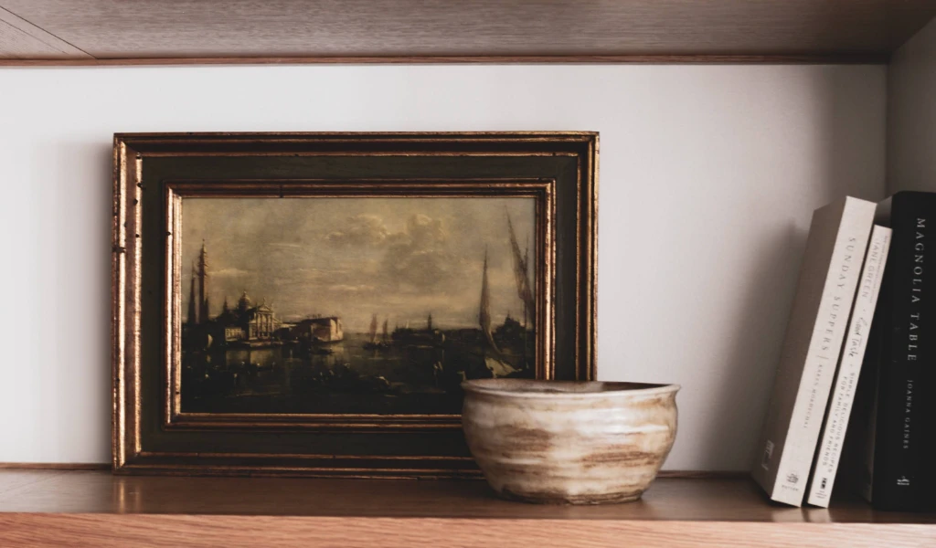 A framed painting and vase on a shelf.
