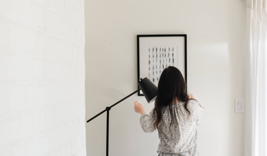 A woman standing in front of a white wall with a framed picture.