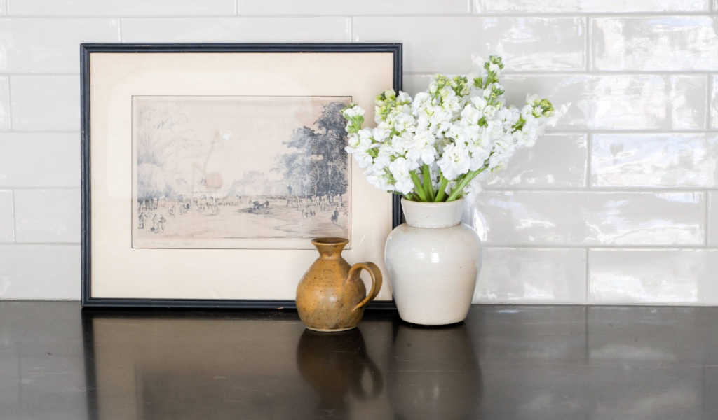 A vase of flowers on a counter next to a framed picture.